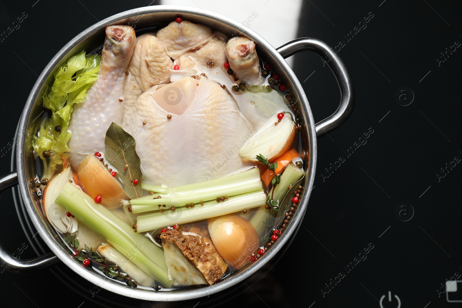 Photo of Whole fresh turkey, cut onion, celery and spices in pot on stove, top view