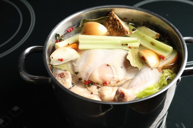 Photo of Whole fresh turkey, cut onion, celery and spices in pot on stove, closeup