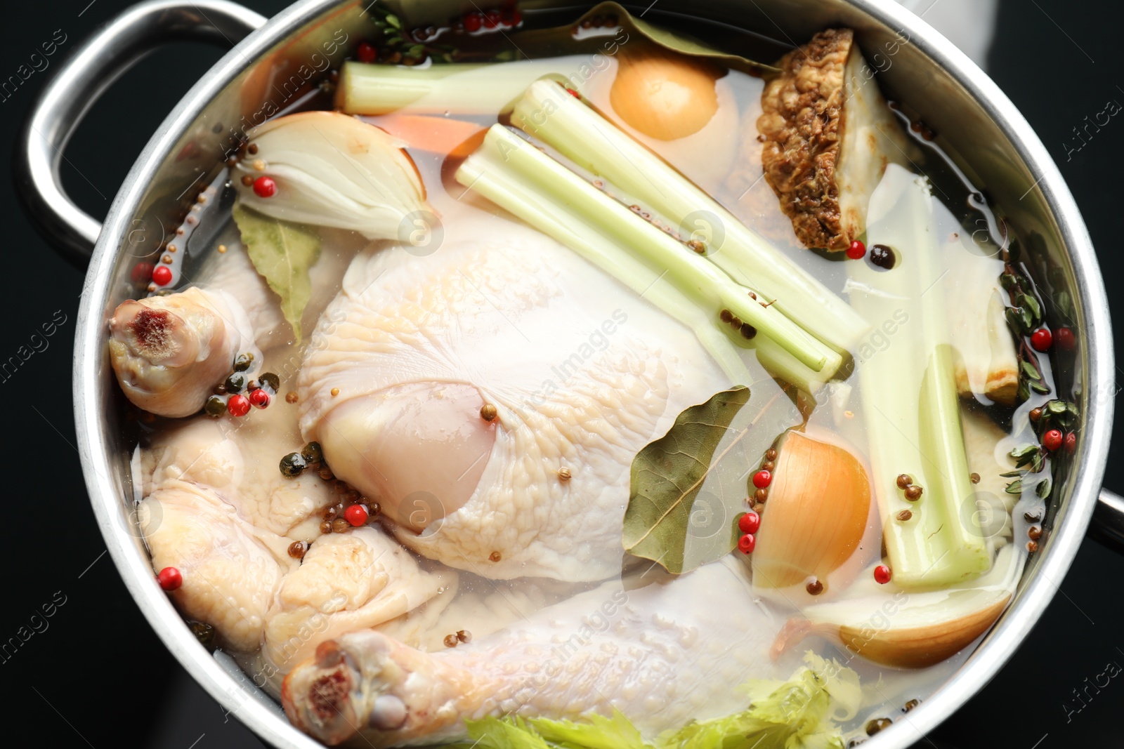 Photo of Whole raw turkey, cut onion, celery and spices in pot, closeup