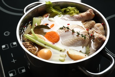 Photo of Whole fresh turkey, cut onion, carrot, celery and spices in pot on stove, closeup