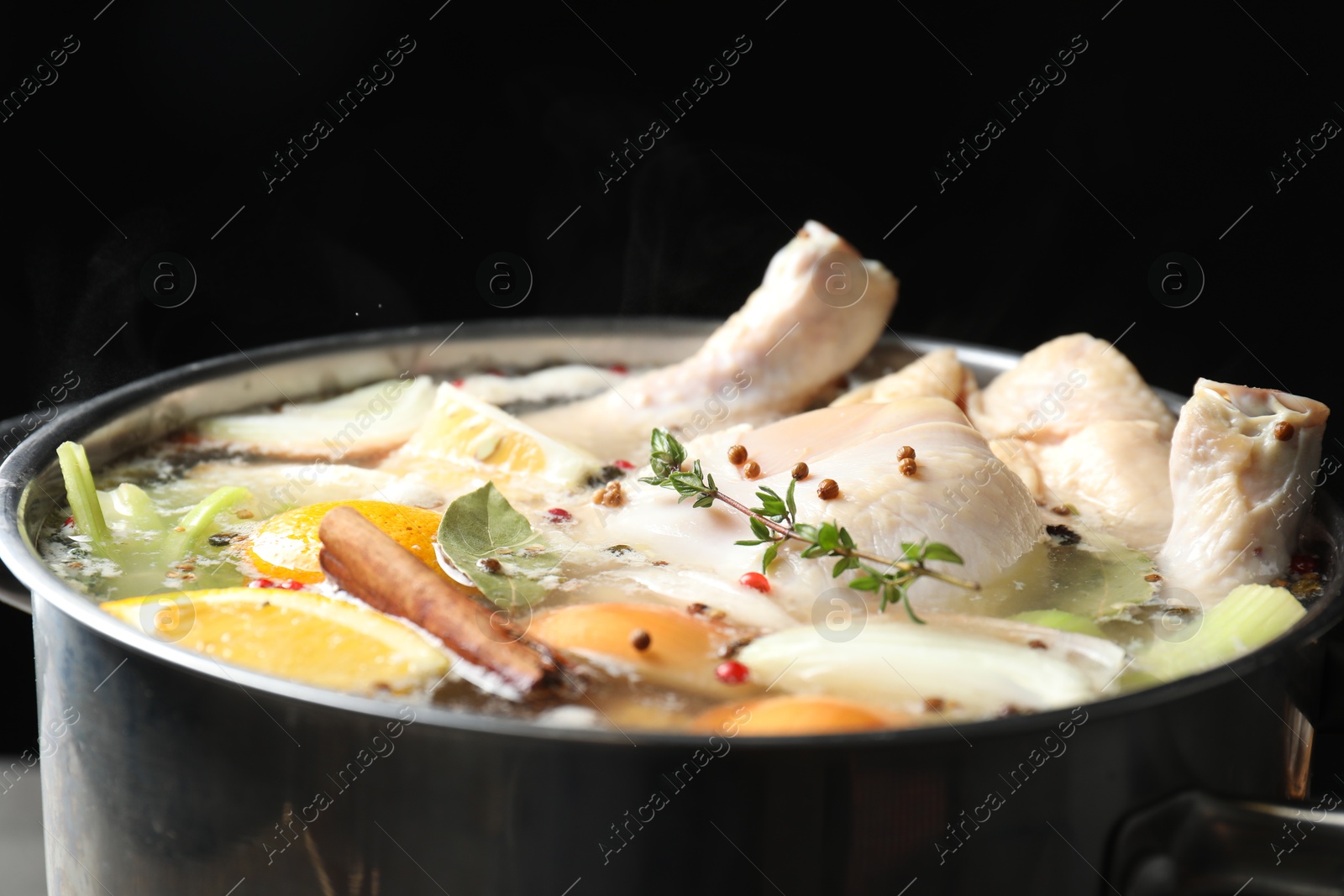 Photo of Whole fresh turkey, cut citrus fruits, thyme and spices boiling in pot against black background, closeup