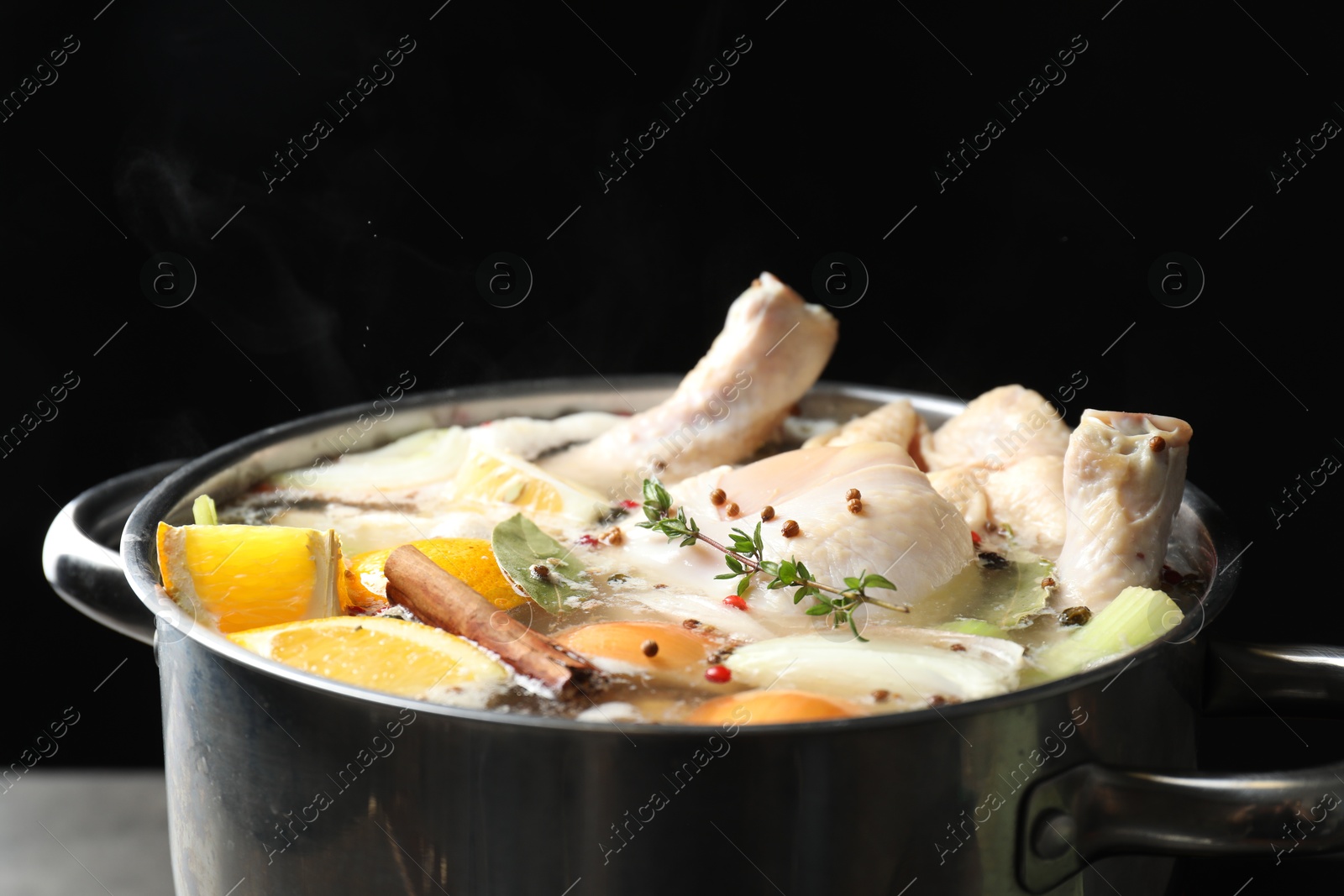 Photo of Whole fresh turkey, cut citrus fruits, thyme and spices boiling in pot on table against black background, closeup