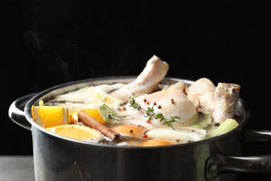 Photo of Whole fresh turkey, cut citrus fruits, thyme and spices boiling in pot on table against black background, closeup