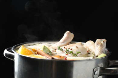 Photo of Whole fresh turkey, cut citrus fruits, thyme and spices boiling in pot on black background, closeup