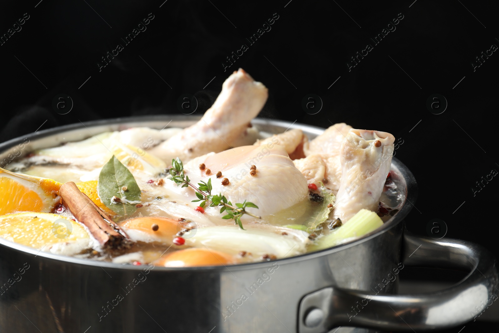 Photo of Whole fresh turkey, cut citrus fruits, thyme and spices boiling in pot on black background, closeup