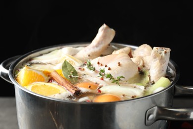 Photo of Whole fresh turkey, cut citrus fruits, thyme and spices boiling in pot on black background, closeup