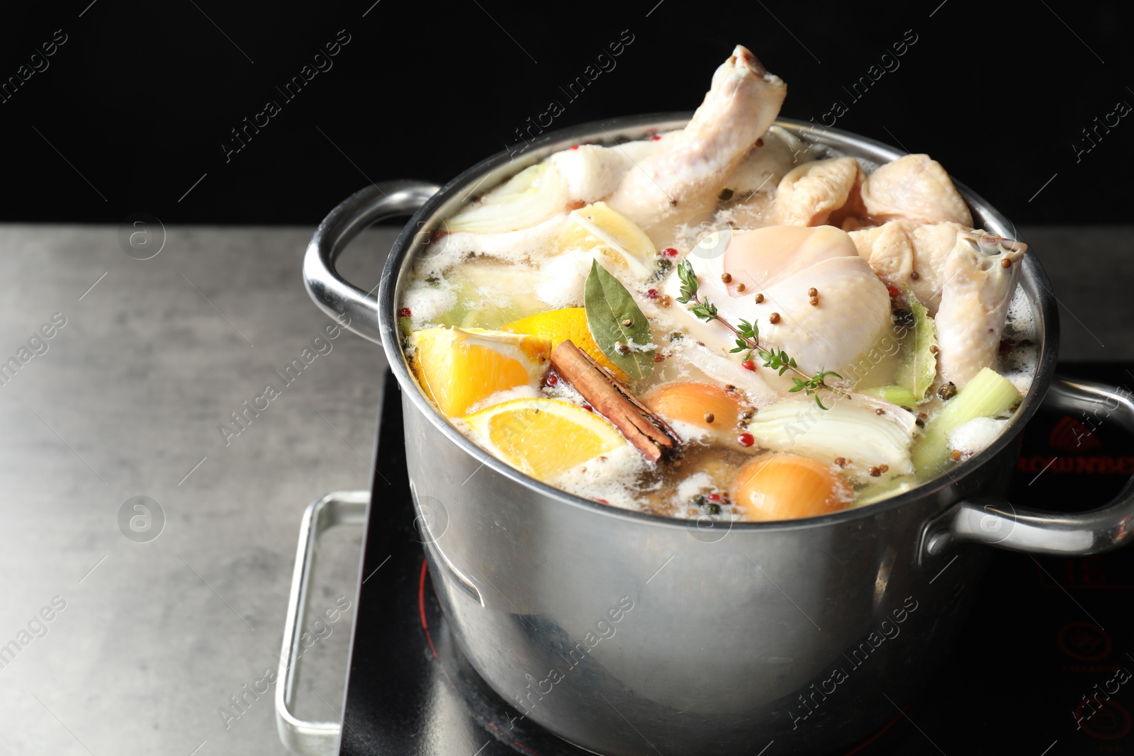 Photo of Whole fresh turkey, cut citrus fruits, thyme and spices boiling in pot on stove on grey table against black background, closeup