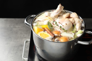 Photo of Whole fresh turkey, cut citrus fruits, thyme and spices boiling in pot on stove on grey table against black background, closeup