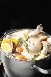 Photo of Whole fresh turkey, cut citrus fruits, thyme and spices boiling in pot on black background, closeup