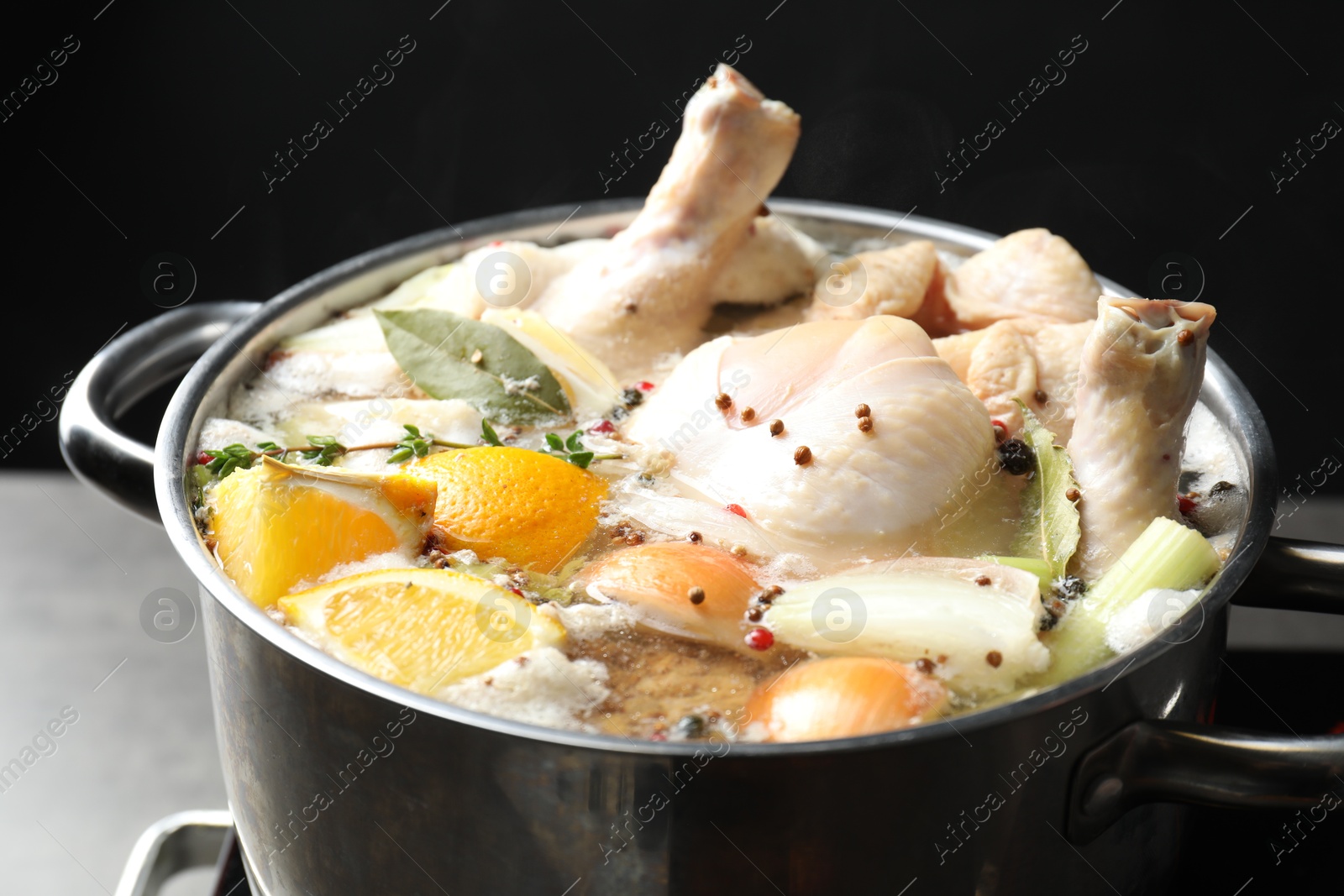 Photo of Whole fresh turkey, cut citrus fruits, thyme and spices boiling in pot on table against black background, closeup