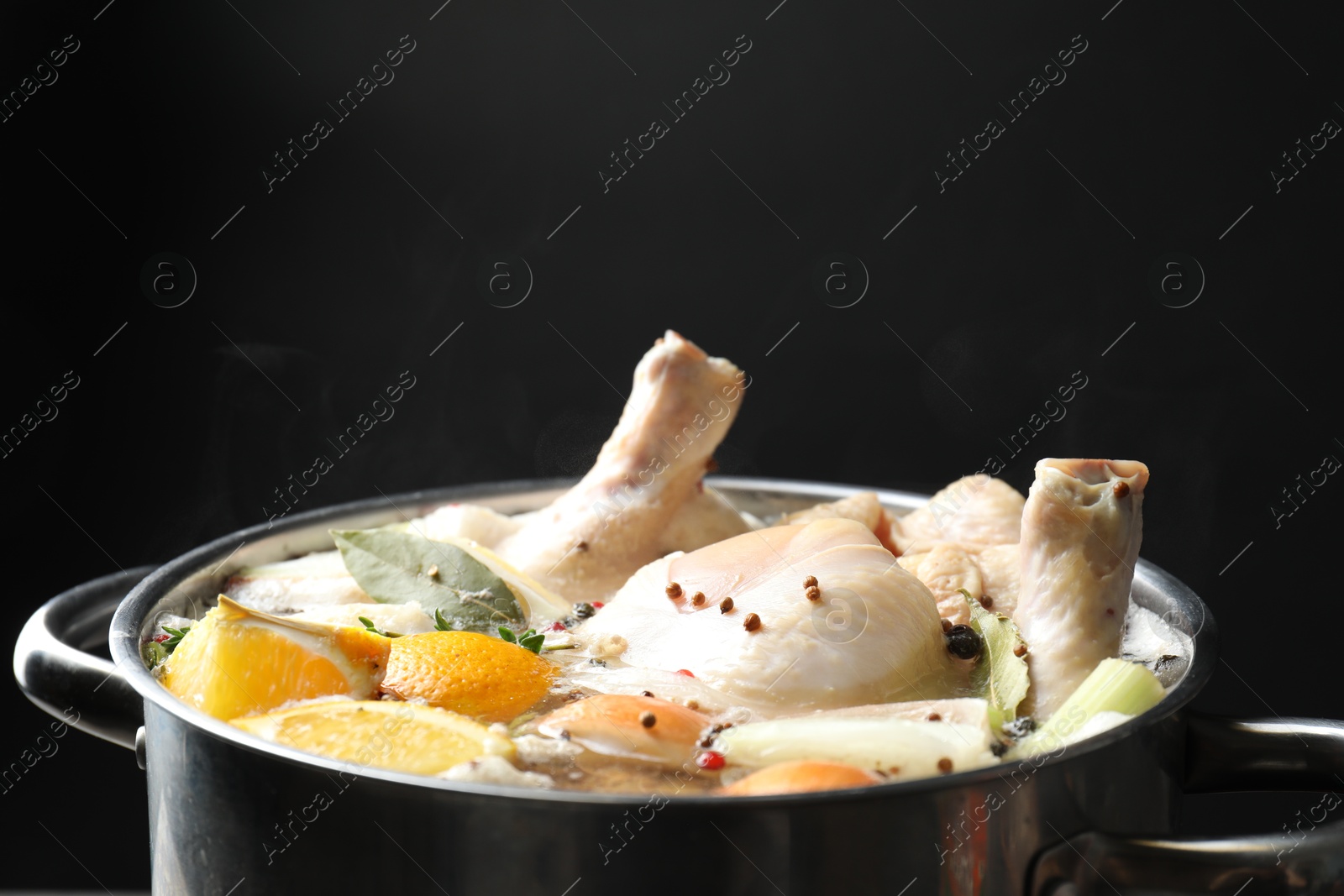 Photo of Whole fresh turkey, cut citrus fruits and spices boiling in pot on black background, closeup