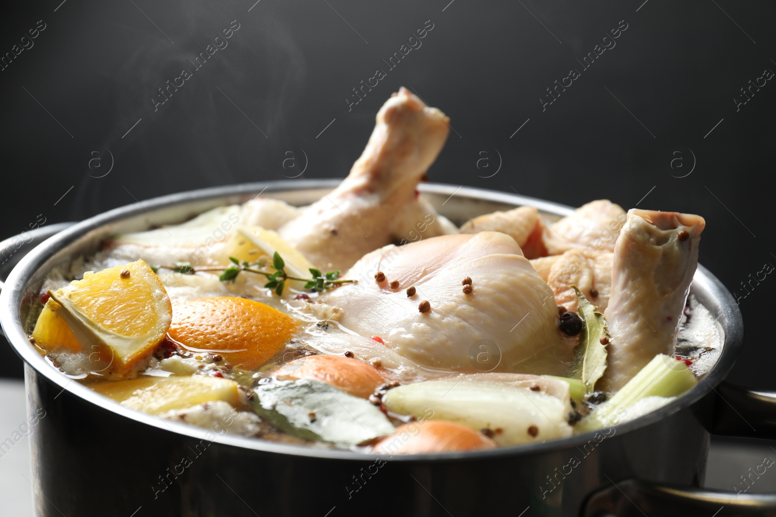 Photo of Whole fresh turkey, cut citrus fruits and spices boiling in pot on table against black background, closeup