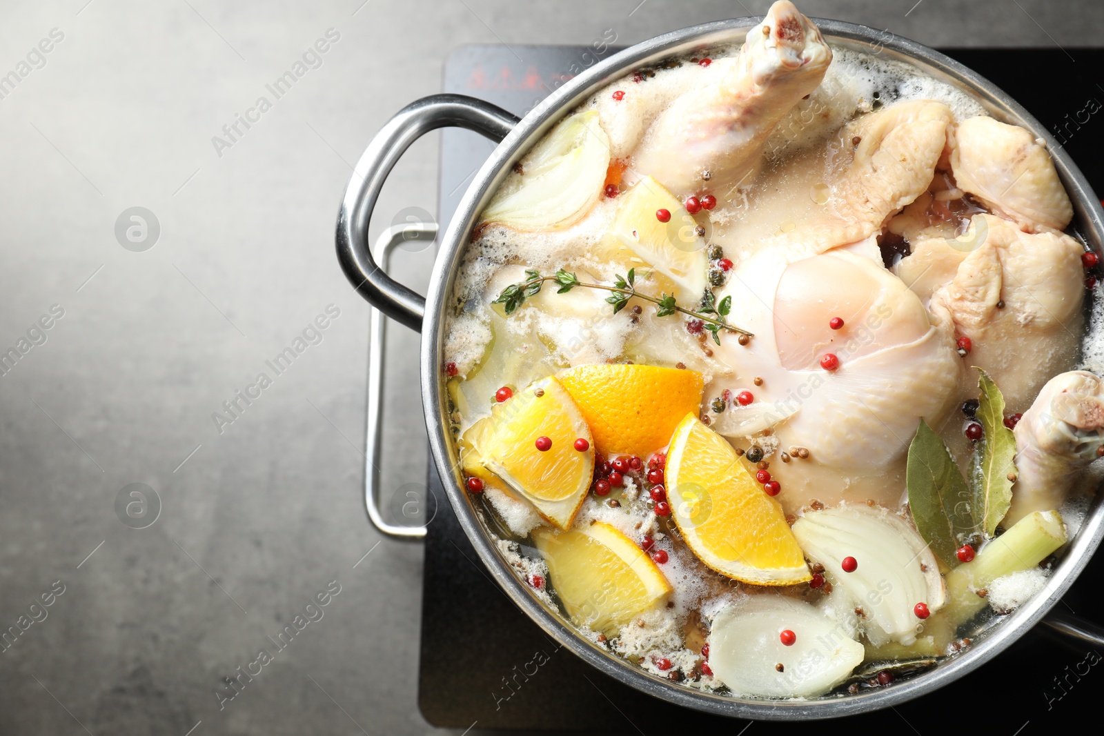 Photo of Whole fresh turkey, cut citrus fruits, thyme and spices boiling in pot on stove on grey table, top view. Space for text