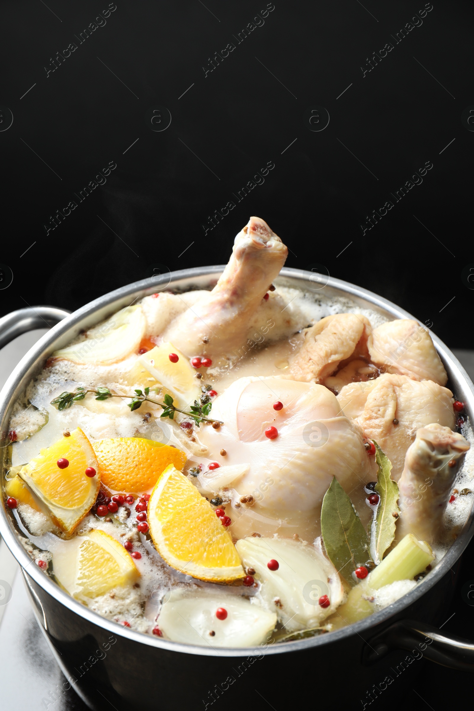 Photo of Whole fresh turkey, cut citrus fruits and spices boiling in pot on black background, closeup