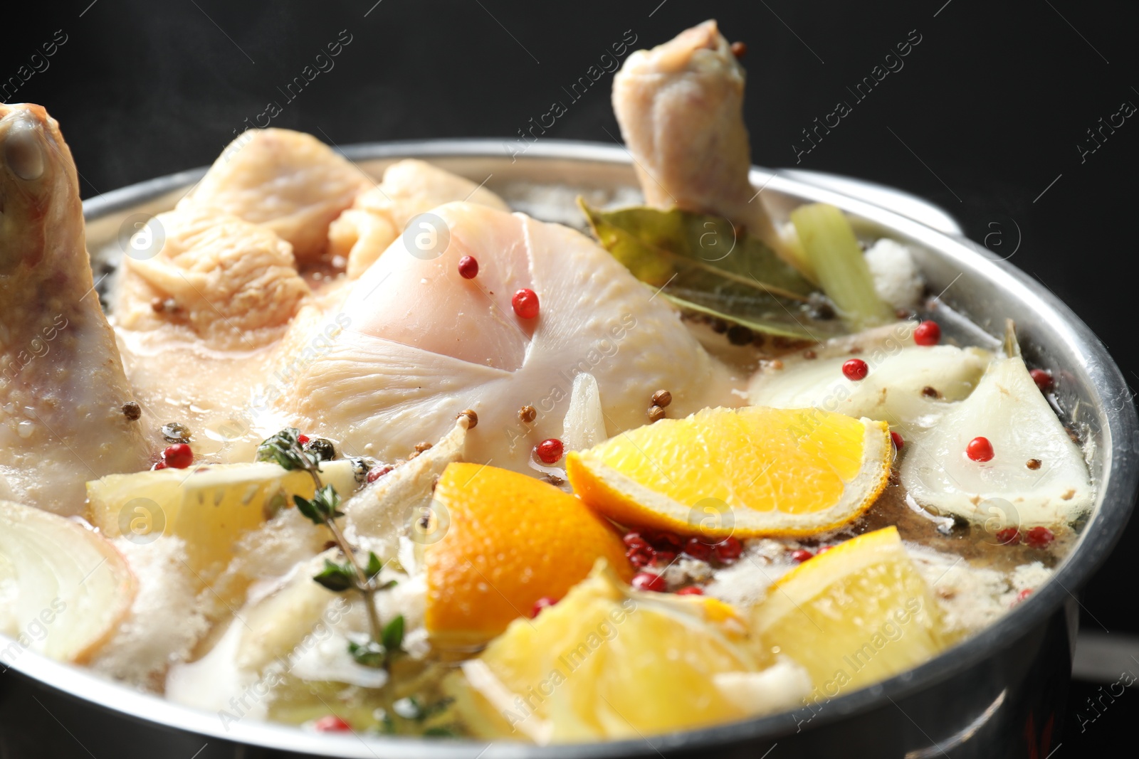 Photo of Whole fresh turkey, cut citrus fruits and spices boiling in pot on black background, closeup