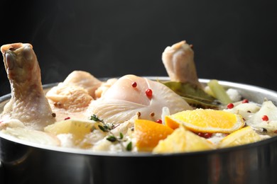 Photo of Whole fresh turkey, cut citrus fruits and spices boiling in pot on black background, closeup