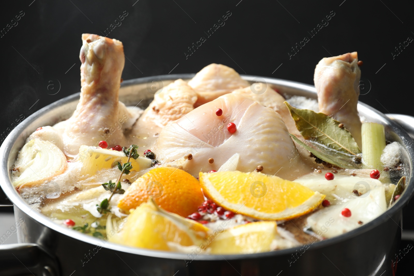 Photo of Whole fresh turkey, cut citrus fruits and spices boiling in pot on black background, closeup