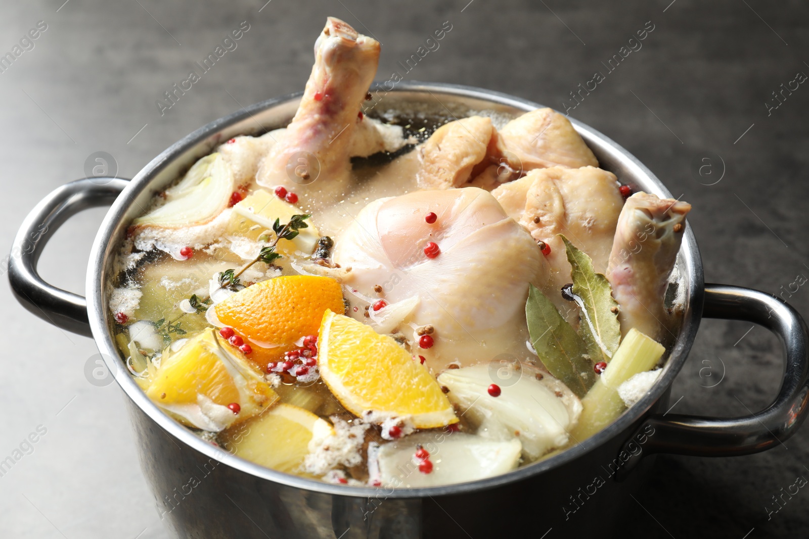 Photo of Whole turkey, cut citrus fruits and spices in pot on grey table, closeup