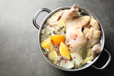 Photo of Whole turkey, cut citrus fruits and spices in pot on grey textured table, top view. Space for text