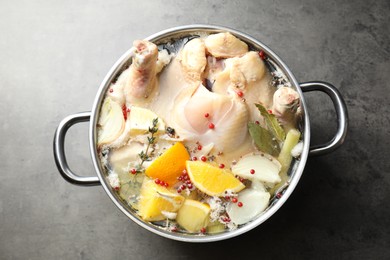 Photo of Whole turkey, cut citrus fruits and spices in pot on grey textured table, top view