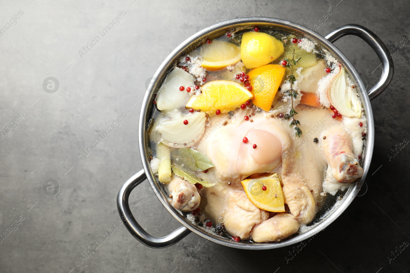 Photo of Whole turkey, cut citrus fruits and spices in pot on grey textured table, top view. Space for text