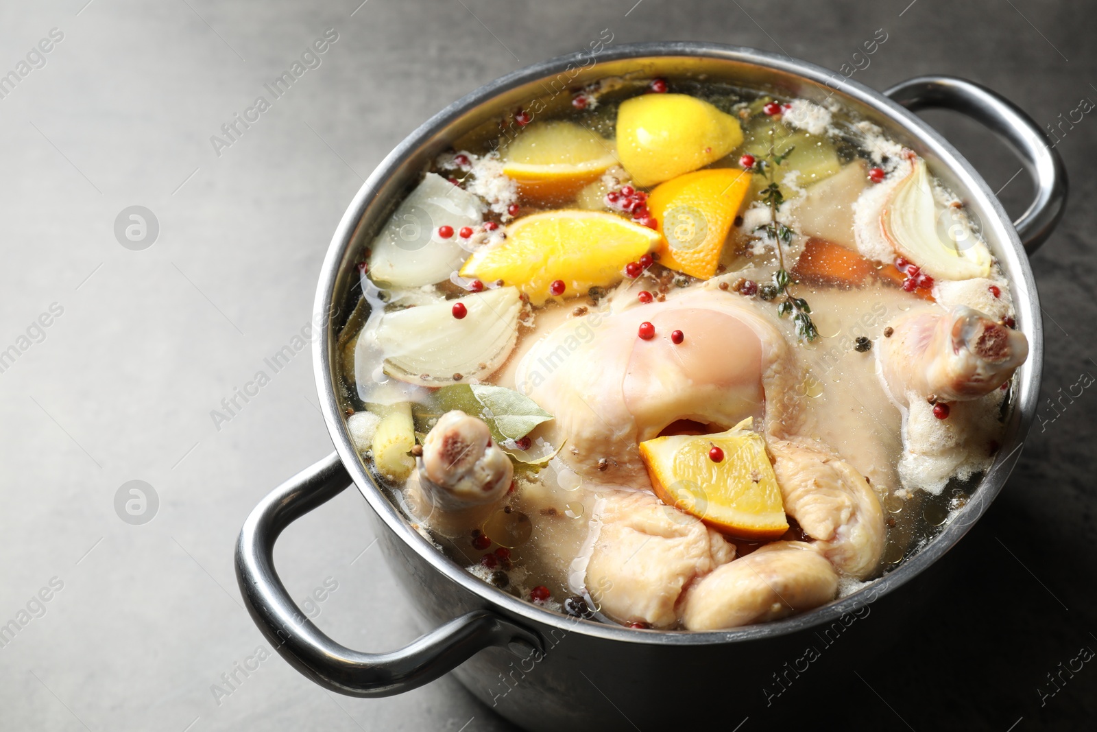 Photo of Whole turkey, cut citrus fruits and spices in pot on grey table, closeup. Space for text