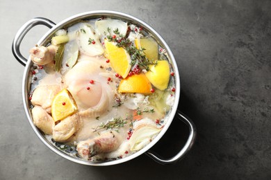 Photo of Whole turkey, cut citrus fruits and spices in pot on grey textured table, top view. Space for text