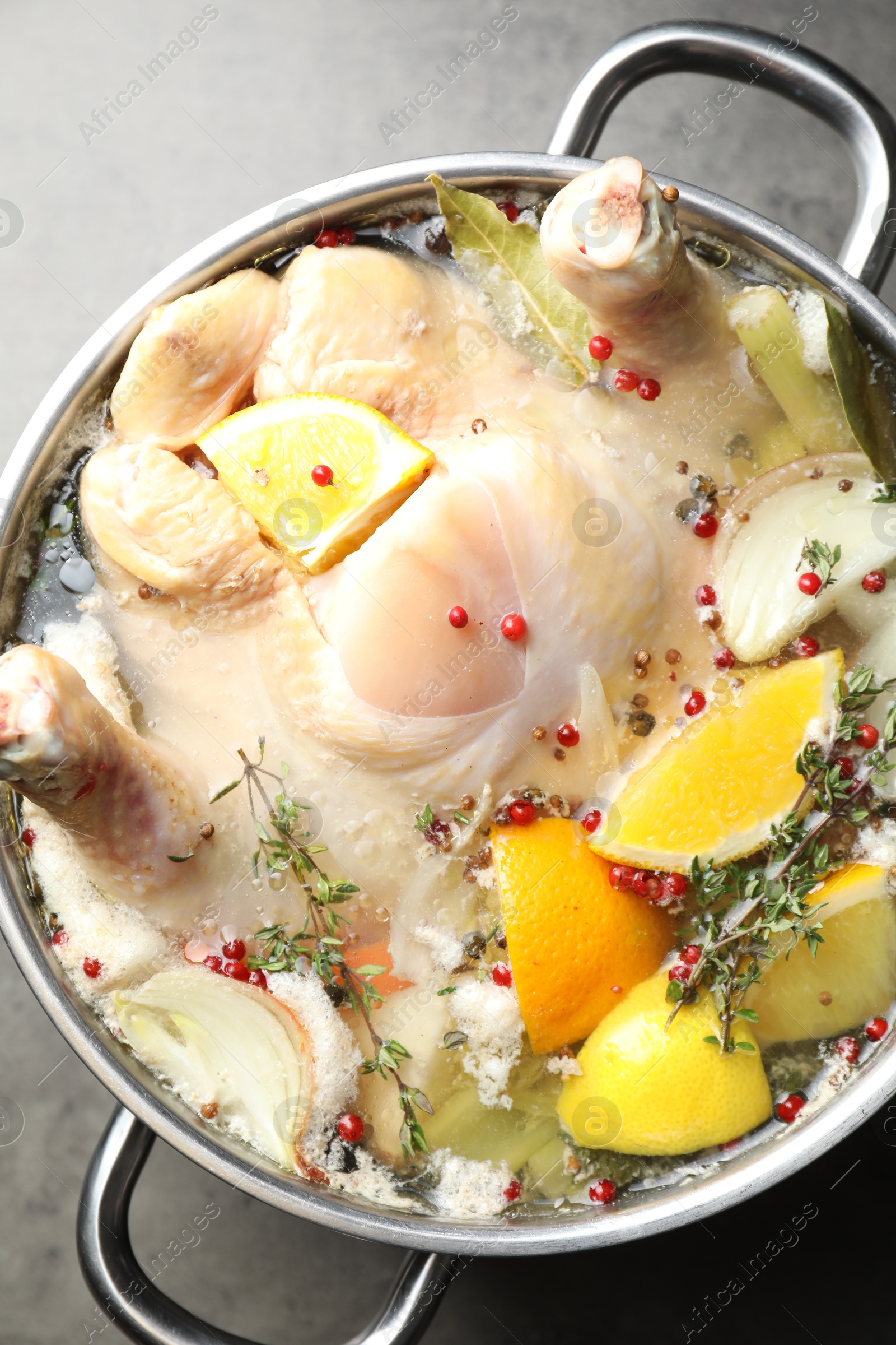 Photo of Whole turkey, cut citrus fruits and spices in pot on grey textured table, top view