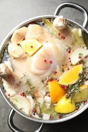 Photo of Whole turkey, cut citrus fruits and spices in pot on grey textured table, top view