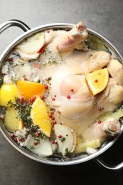 Photo of Whole turkey, cut citrus fruits and spices in pot on grey textured table, top view