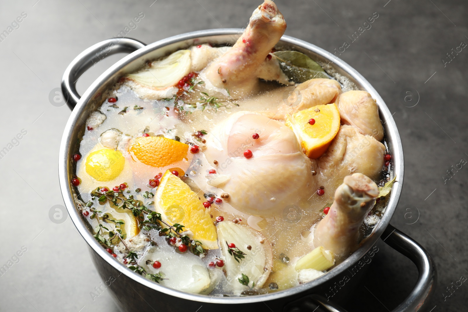 Photo of Whole turkey, cut citrus fruits and spices in pot on grey table, closeup