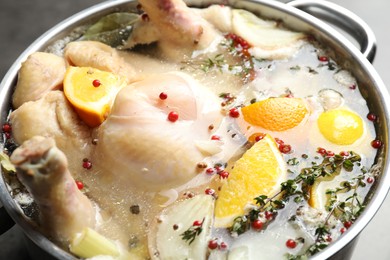 Photo of Whole turkey, cut citrus fruits and spices in pot on table, closeup