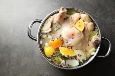 Photo of Whole turkey, cut citrus fruits and spices in pot on grey textured table, top view. Space for text