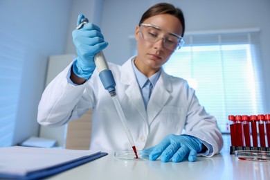 Photo of Laboratory testing. Doctor dripping blood sample into Petri dish at table indoors, selective focus