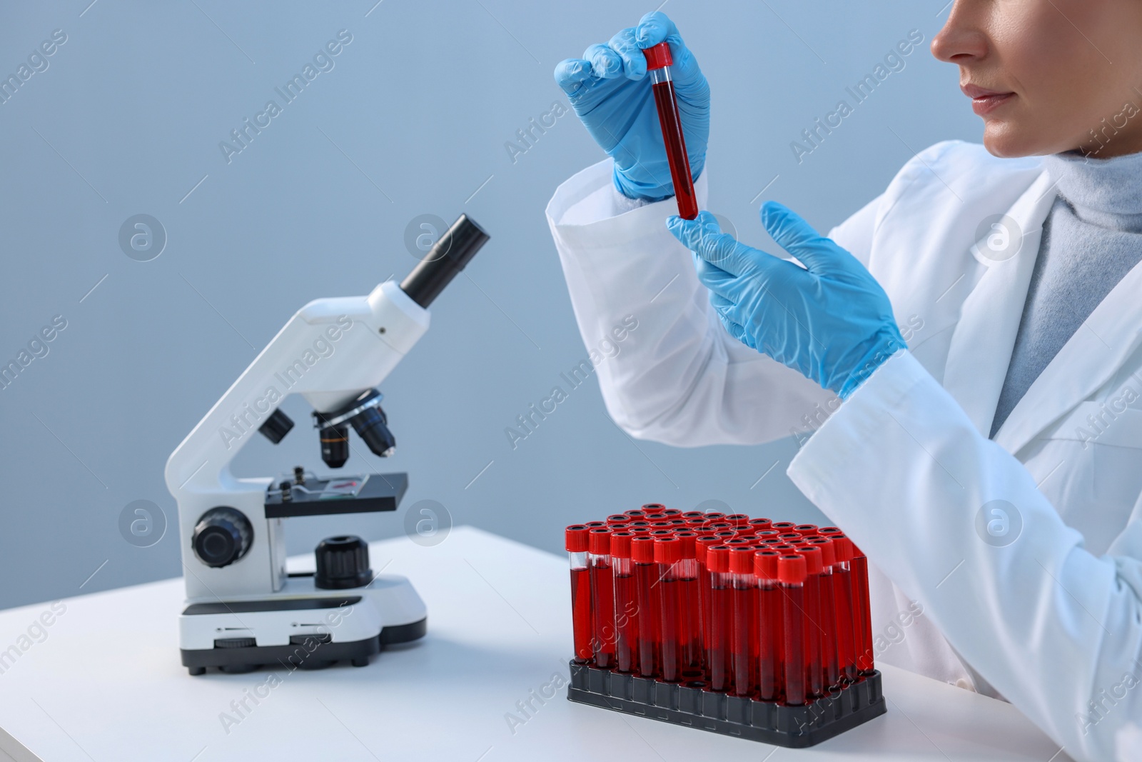 Photo of Laboratory testing. Doctor holding test tube with blood sample at table indoors, closeup