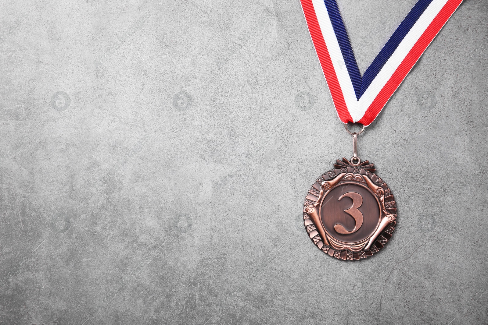 Photo of Bronze medal with striped ribbon on grey background, top view. Space for text