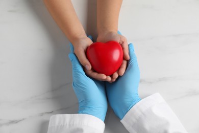 Photo of Doctor and child with heart model at white marble table, top view