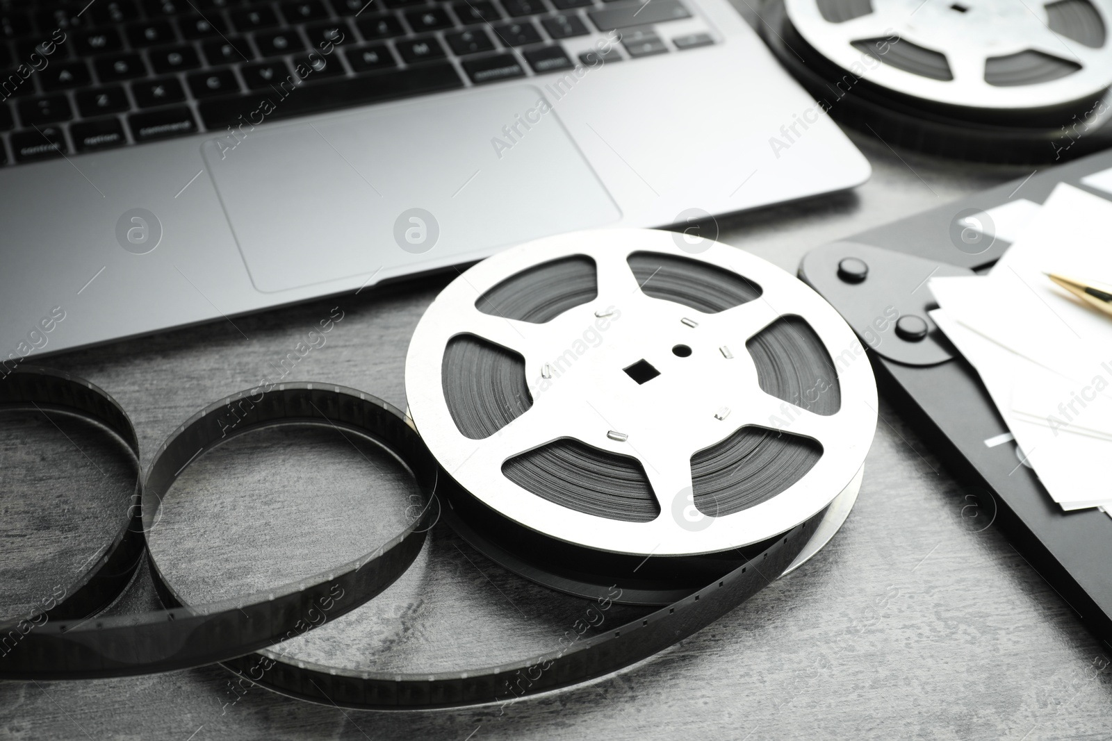 Photo of Film reels and laptop on grey textured table, closeup