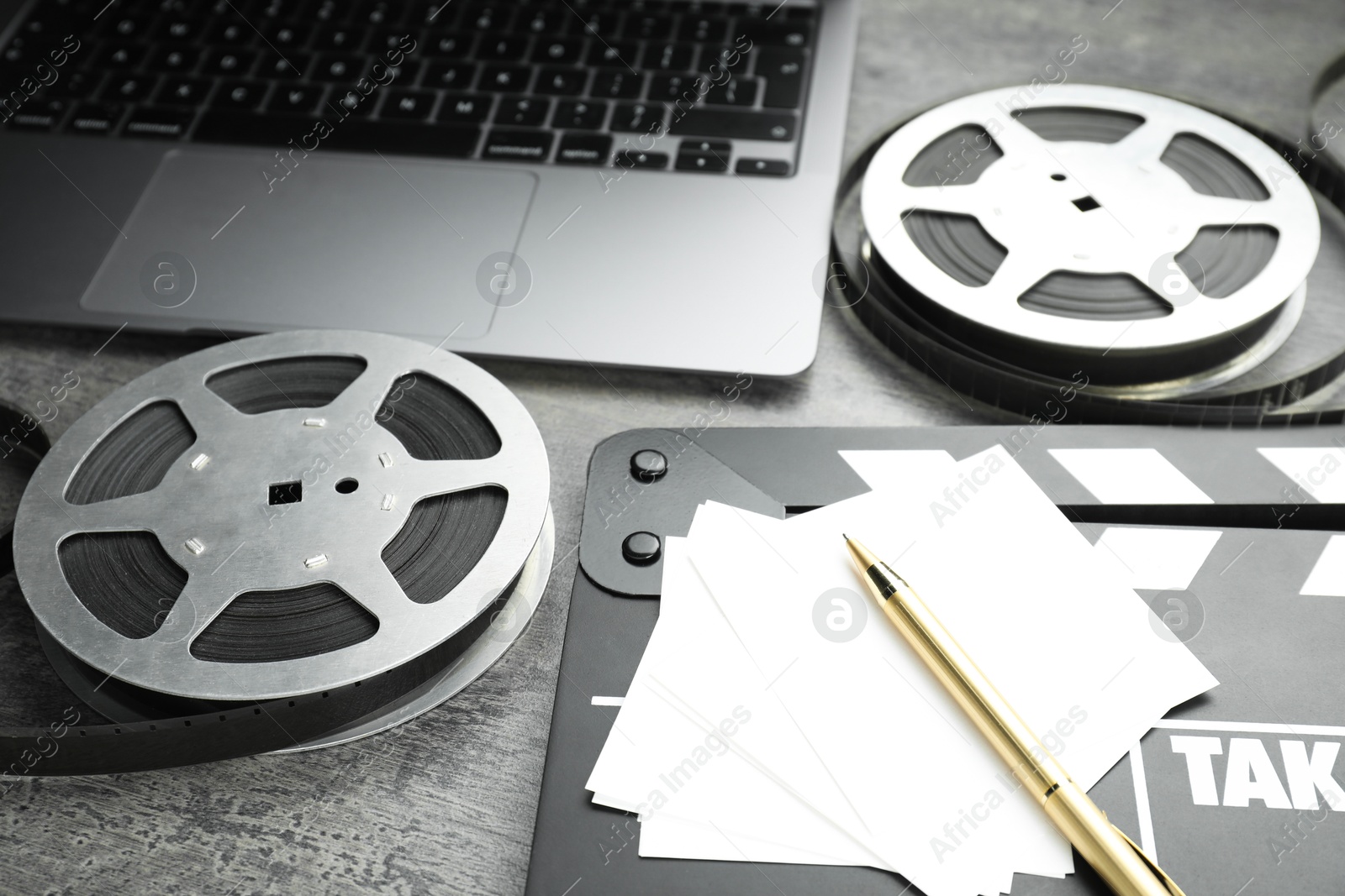 Photo of Movie clapper, paper notes, pen, film reels and laptop on grey textured table, closeup