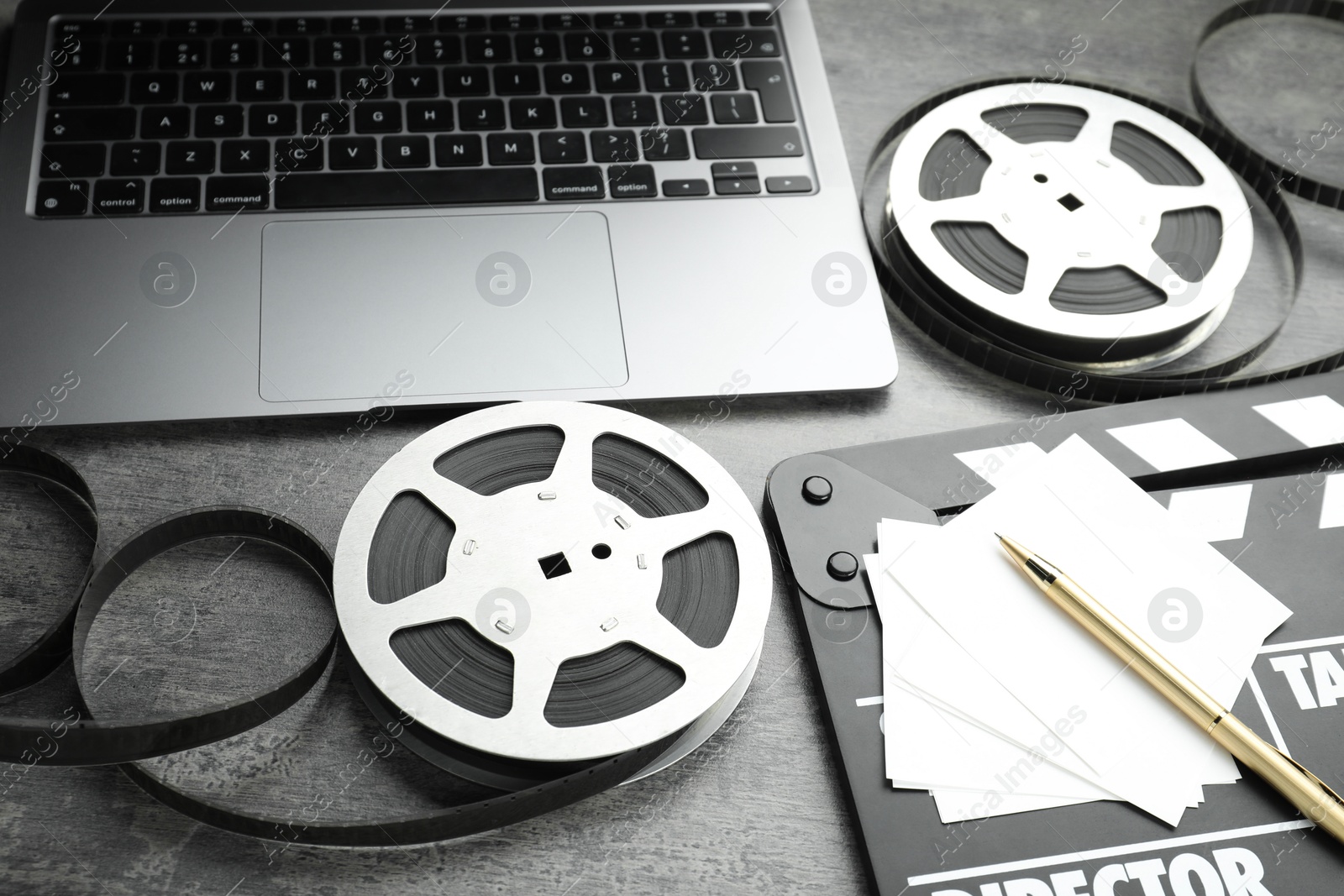 Photo of Movie clapper, paper notes, pen, film reels and laptop on grey textured table