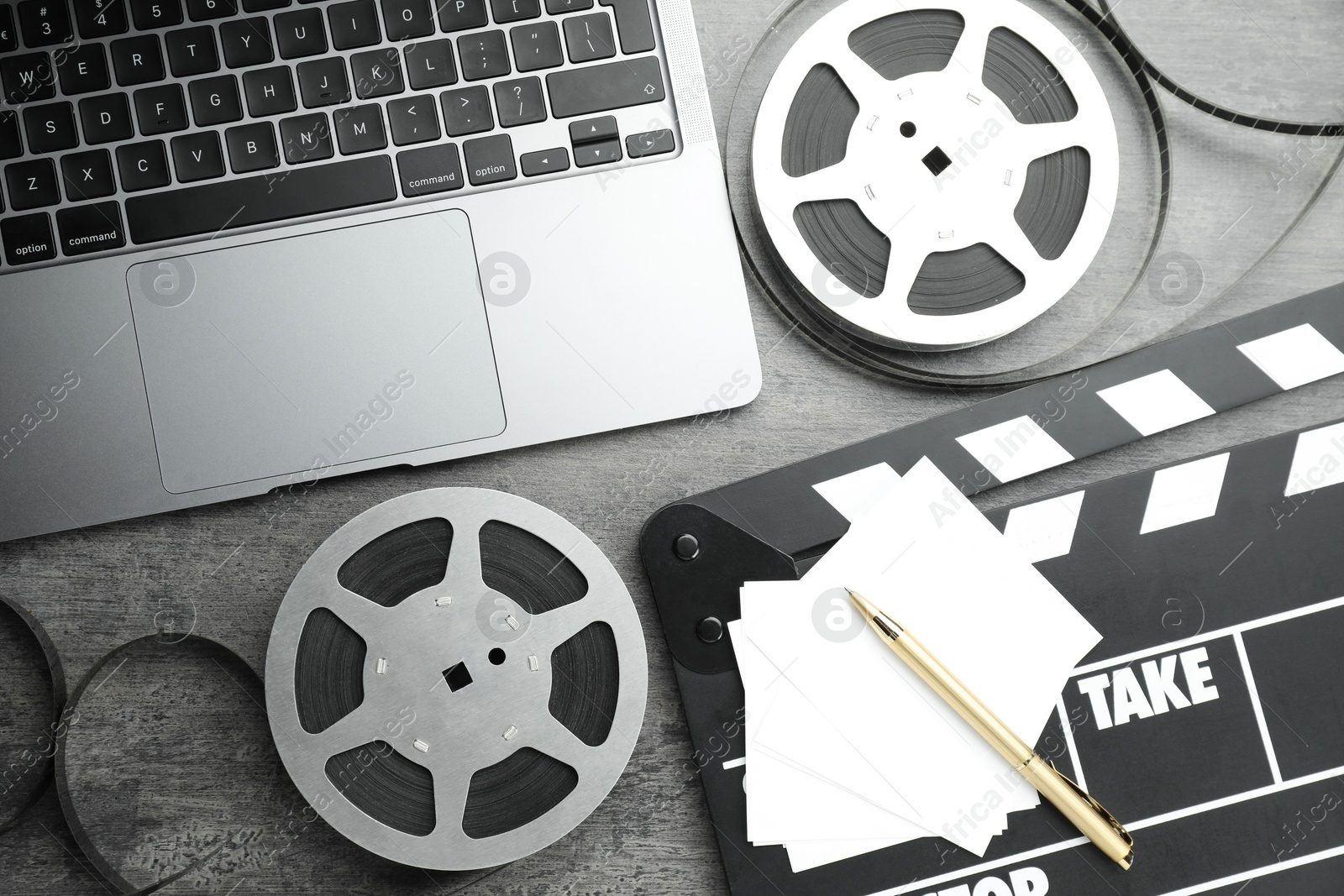 Photo of Flat lay composition with movie clapper, film reels and laptop on grey textured table