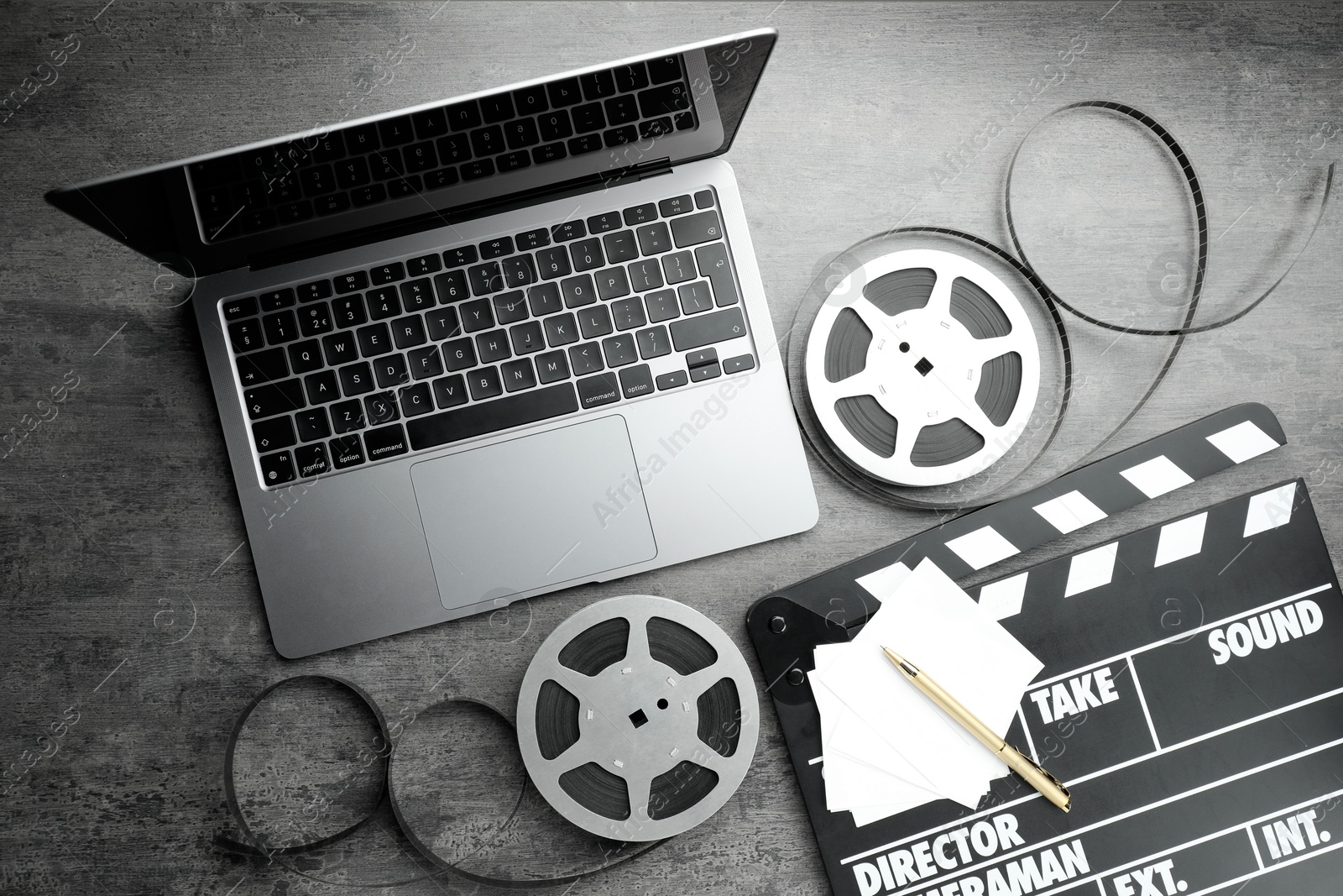 Photo of Flat lay composition with movie clapper, film reels and laptop on grey textured table