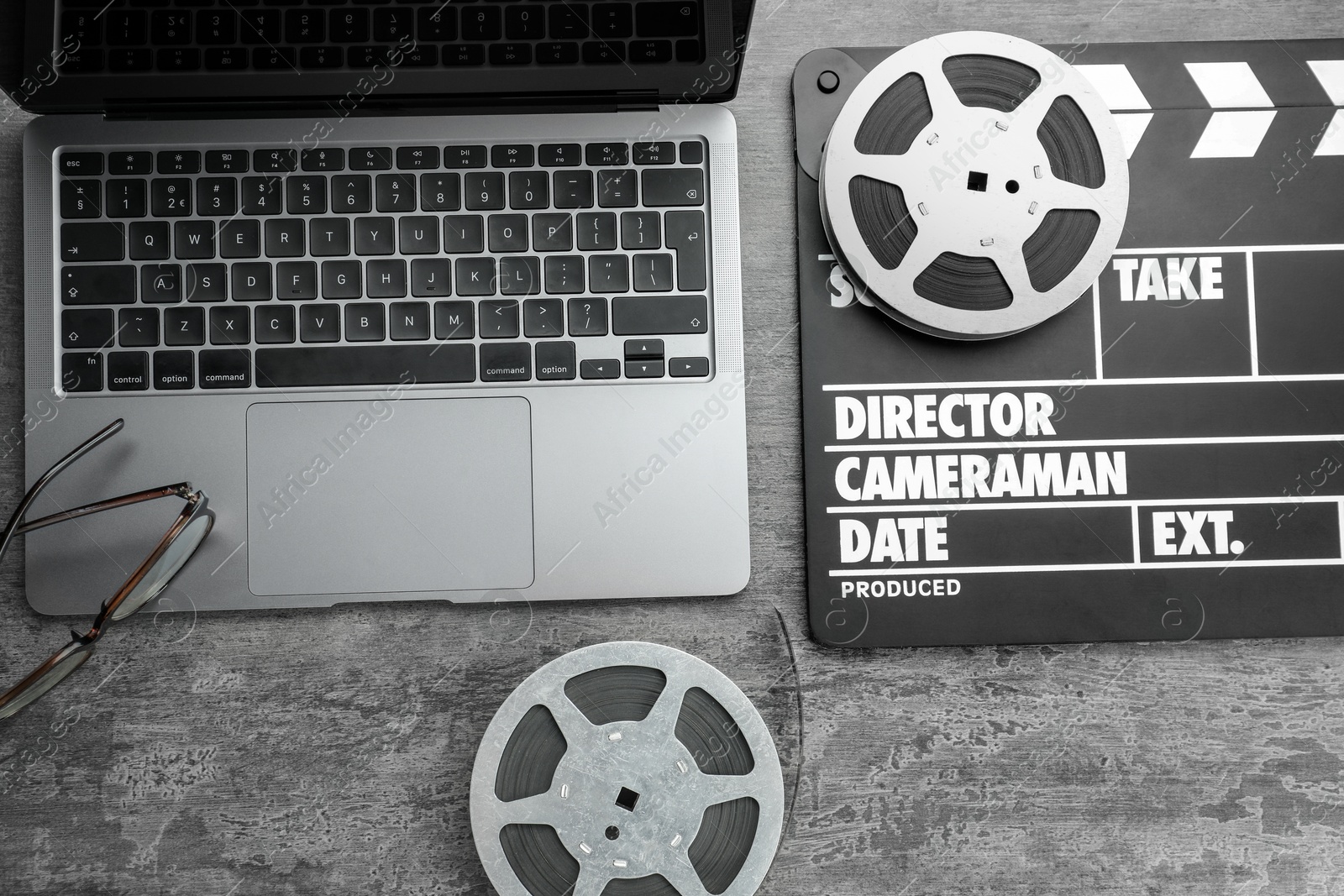 Photo of Movie clapper, film reels and laptop on grey textured table, flat lay