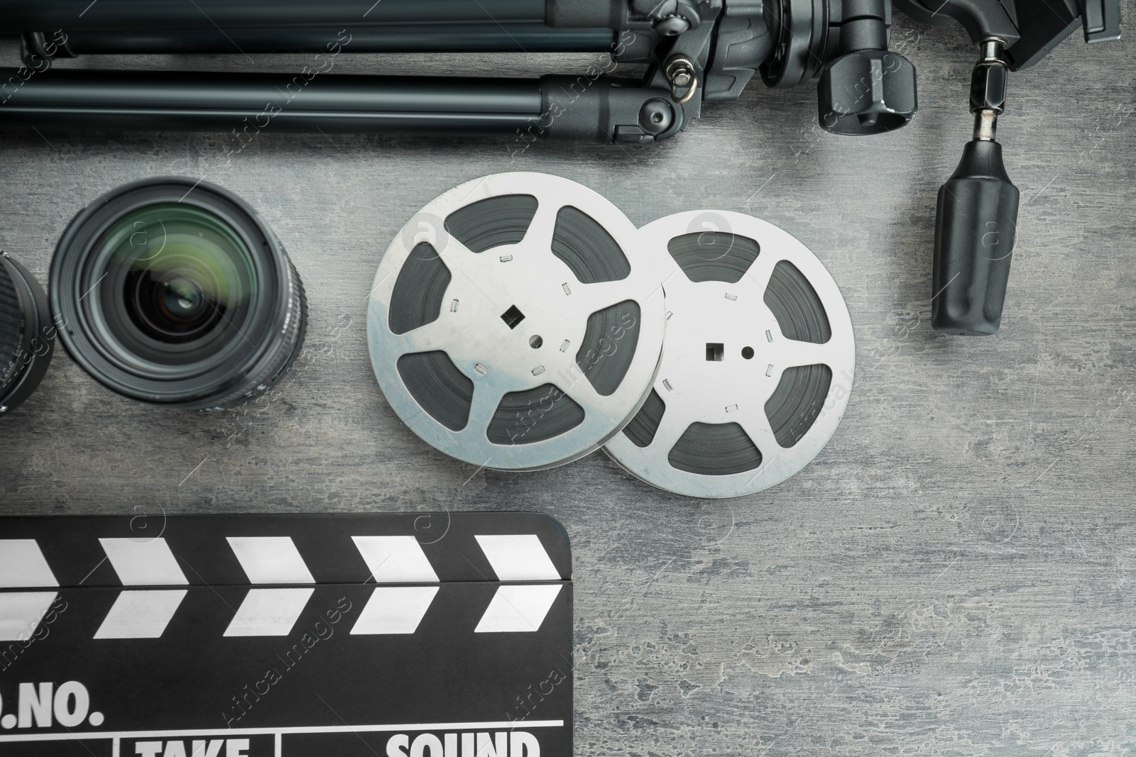 Photo of Flat lay composition with movie clapper, film reels and camera lens on grey textured table