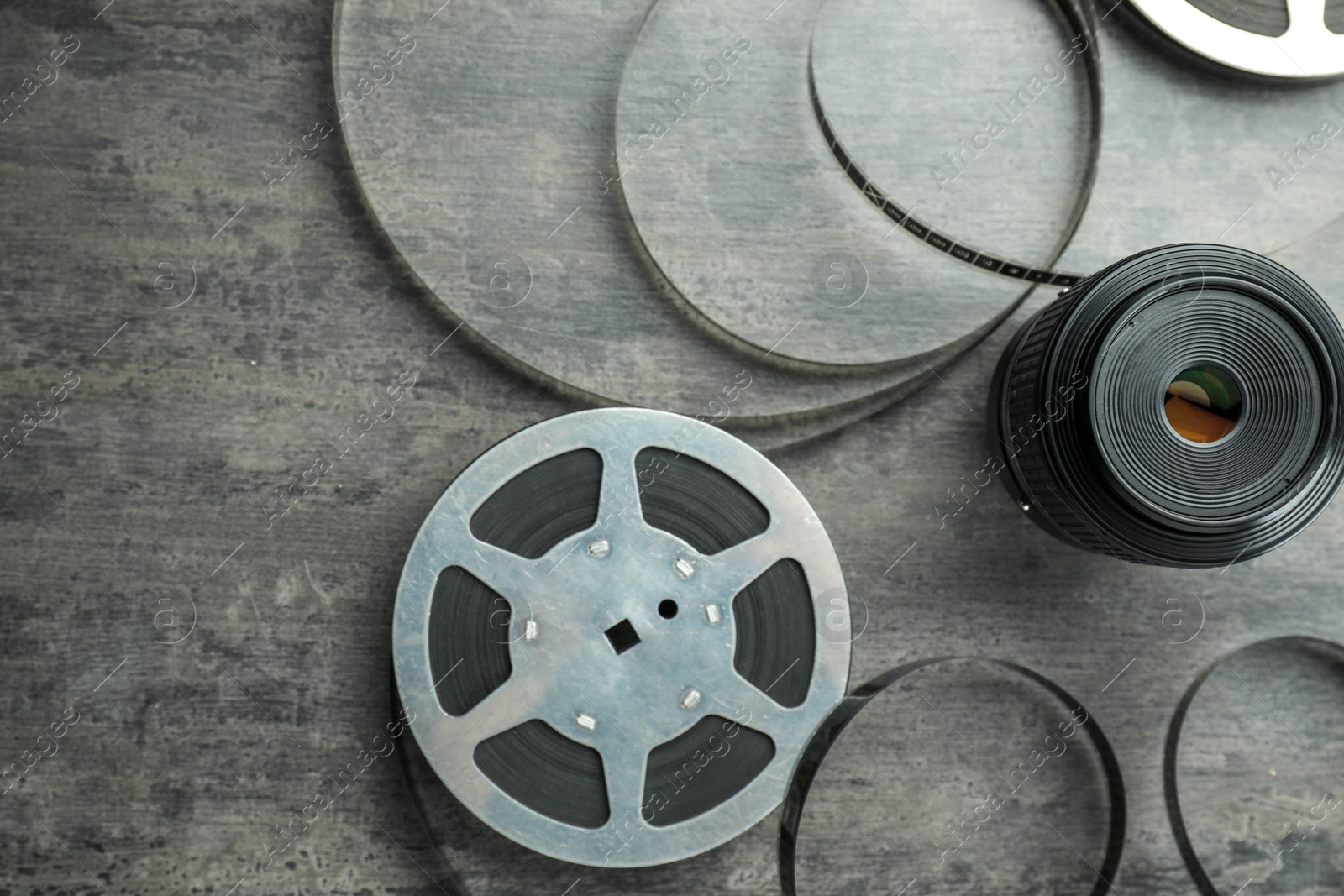 Photo of Film reel and camera lens on grey textured table, flat lay