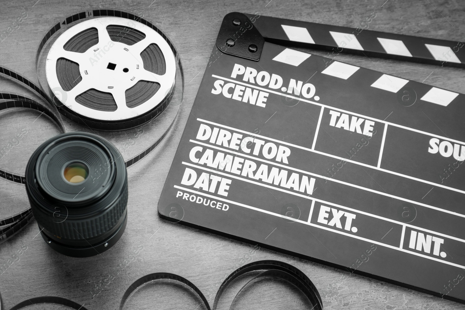 Photo of Movie clapper, film reel and camera lens on grey textured table