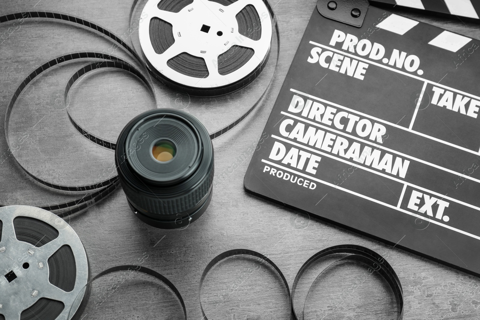 Photo of Movie clapper, film reels and camera lens on grey textured table, above view