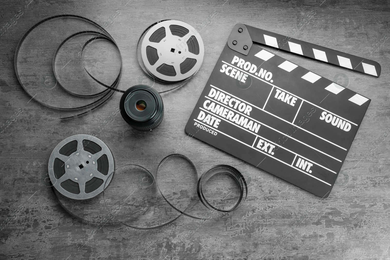 Photo of Flat lay composition with movie clapper, film reels and camera lens on grey textured table