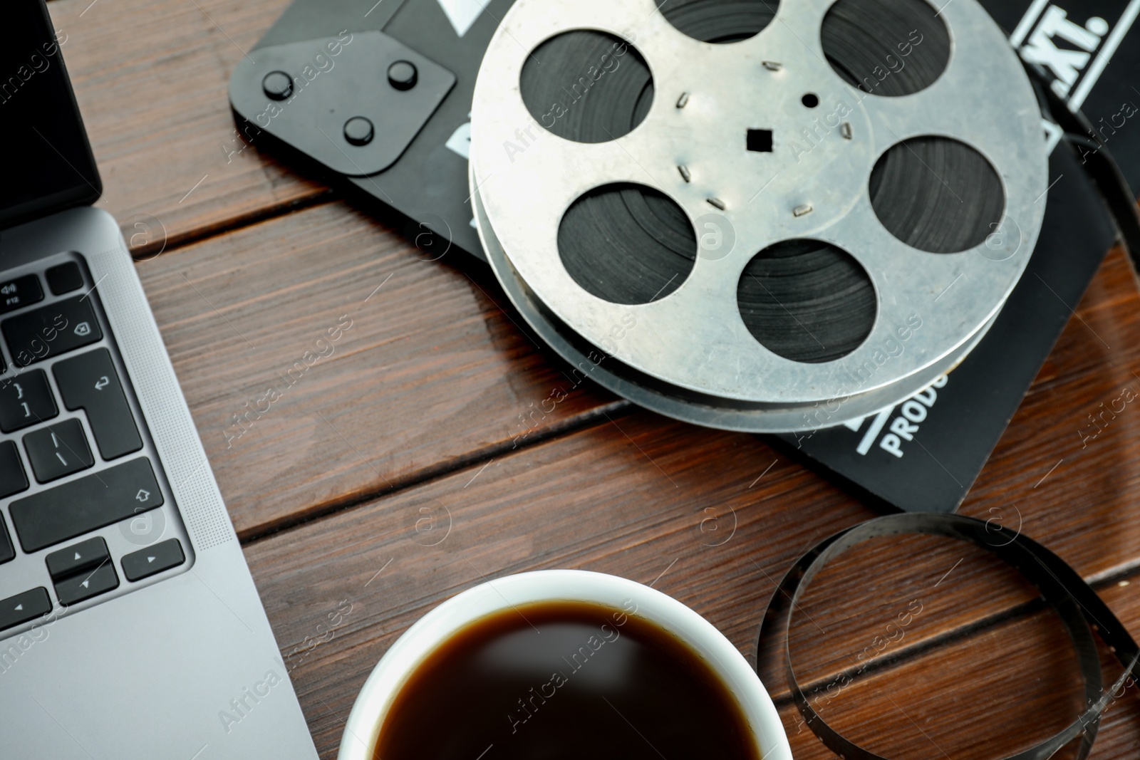 Photo of Movie clapper, laptop and film reel on wooden table, above view