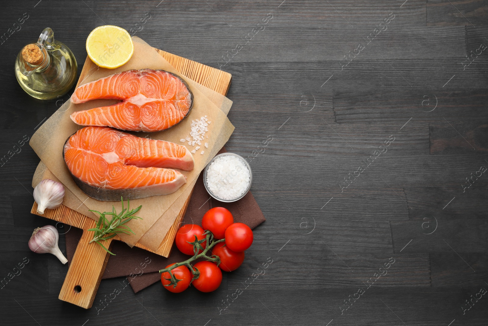 Photo of Fresh raw salmon steaks and products on black wooden table, flat lay. Space for text